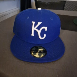 Blå New Era 59FIFTY KC keps - Snygg blå 59FIFTY keps från New Era med KC-logga i vitt framtill. Officiell MLB Authentic Collection, med broderade detaljer och klassisk flat skärm. Perfekt för dig som gillar baseball eller vill ha en sportig look.
