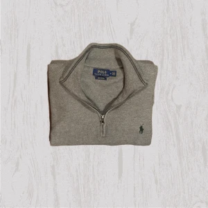 Grå  half zip tröja från Polo Ralph Lauren - Snygg grå tröja från Polo Ralph Lauren med half zip och klassisk krage. Tröjan har lång ärm och den ikoniska gröna loggan broderad på bröstet. Perfekt för lager-på-lager och chill stil. Materialet är mjukt och skönt, passar till många outfits.