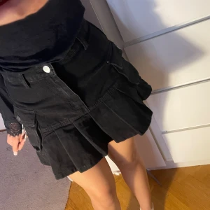 Svart minikjol  - Trendig svart kjol i denimstil med veck och sidfickor. Sitter snyggt i midjan och ger en lite Y2K/utility look. Perfekt att styla med boots eller sneakers! Storlek: S Fint skick, ej använd.  🖤 Must-have för hösten och supertrendig året runt!