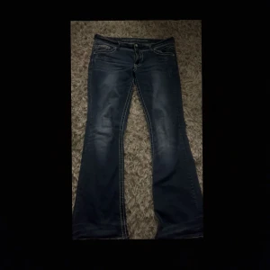 Blå bootcut jeans med broderade fickor miss me liknade  - Snygga mörkblå jeans från Vanity med bootcut passform och markerade kontrastsömmar. Bakfickorna är dekorerade med broderier och nitar som ger extra edge. Jeansen har klassisk femficksdesign och dragkedja framtill. Köpte de i usa för 100$ pris går altid att diskutera 