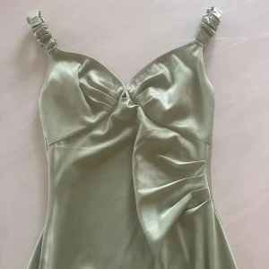 Ljusgrön satin klänning från Adoore - Supersnygg ljusgrön långklänning från Adoore i satin med omlottdetaljer framtill och rynkade axelband. Klänningen har en elegant v-ringning och ett mjukt, glansigt material som ger en lyxig känsla. Använd en gång .