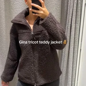 Mörkbrun teddyjacka från Gina Tricot - Mysig mörkbrun teddyjacka från Gina Tricot med dragkedja framtill och hög krage. Jackan har en fluffig och mjuk struktur som ger en cool och avslappnad vibe. Perfekt för kyliga dagar när du vill vara både varm och snygg.