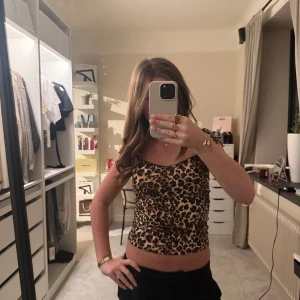 Leopardmönstrad croppad topp från Nelly - Säljer en croppad leopardmönstrad topp från Nelly i storlek S. Toppen har smala axelband, v-ringad hals och svarta spetsdetaljer längs kanten. Materialet är mjukt och stretchigt, perfekt för att skapa en cool och trendig look.