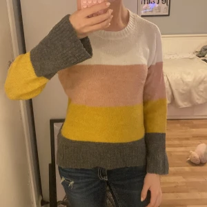 Randig stickad tröja från H&M - Supermysig stickad tröja från H&M med breda ränder i vitt, rosa, gult och mörkgrått. Tröjan har rund halsringning och långa ärmar med ribbade muddar. Perfekt för dig som gillar färg och vill ha en chill look.