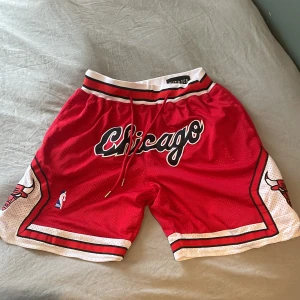 Chicago Bulls Just Don basketshorts - Säljer ett par röda Chicago Bulls basketshorts från Just Don, inspirerade av 1997-98 säsongen. Shortsen har broderad logga, snörning i midjan, vita och svarta detaljer samt meshmaterial för extra komfort. Perfekta för dig som älskar basket och streetwear.