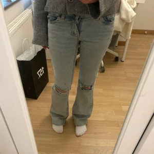 Nelly jeans med slitningar  - Säljer ett par ljusblå Nelly jeans med bootcut passform och snygga slitningar på knäna. Jeansen har klassisk femficksdesign och en rosa broderad detalj på bakfickan. OBS dom är i den kortare modellen.