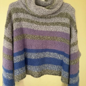 Randig gosig polotröja i lila/ blått/grått - Mysig polotröja med ränder i lila, blått och grått. Tröjan har en loose passform, långärmade ärmar och är stickad i ett supermjukt material. Polokragen är extra bred och kan draperas eller vikas på olika sätt.