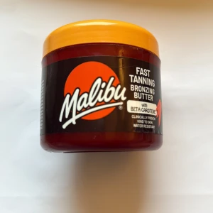 Malibu Fast Tanning Bronzing Butter - Malibu Fast Tanning Bronzing Butter med beta-caroten ger huden en solkysst ton snabbt. Smöret kommer i en brun plastburk med orange lock och är vattenresistent. Perfekt för dig som vill ha en bronzig glow på kroppen. 70% kvar 
