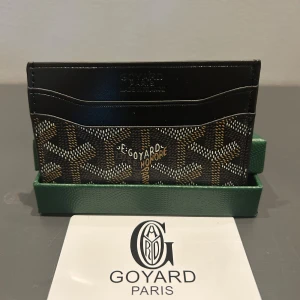  svart plånbok med mönster - Slimmad och stilren plånbok  i svart färg med klassiskt grafiskt mönster i brunt, beige och vitt. Insidan är gul och har flera fack för kort. Perfekt för dig som vill ha en lyxig och unik accessoar med Paris-vibe.