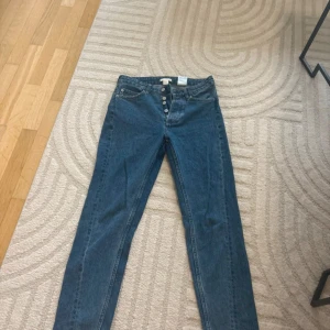 Blå high waist jeans med knappar - Snygga blå jeans från H&M med hög midja och raka ben. Klassisk femficksmodell med silverfärgade knappar i gylfen. Jeansen har en enkel, clean look och är gjorda i slitstarkt denimtyg. Perfekta för dig som gillar en tidlös stil.