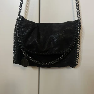 Svart axelväska med kedjedetaljer - Cool svart axelväska i mockaliknande material med glansig finish och kedjedetaljer i metall. Väskan har ett lock med dekorativ kedja och insidan är fodrad med leopardmönstrat tyg. Perfekt för dig som gillar edgy stil och snygga detaljer. Jag är öppen för prisförslag!🩷
