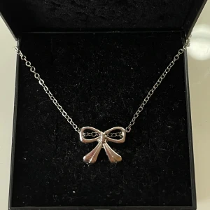 Sött halsband med rosett🎀 - Ett stilrent halsband i silverfärgad metall med en gullig rosett som hänge. Kedjan är tunn och smidig, perfekt för att ge en extra touch till din outfit. Rosetten har en blank finish som fångar ljuset snyggt. Ej riktigt silver.