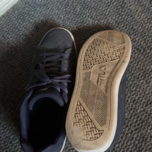 Blå Fila sneakers med snörning - Snygga blåa sneakers från Fila med klassisk låg profil och rund tå. Skorna har vit sula och Fila-logga på sidan. Materialet är syntet med textilfoder och snörning framtill för en skön passform. Perfekt för dig som gillar stilrena och sportiga skor.