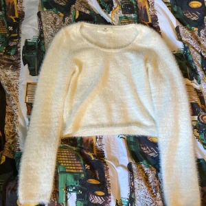 Vit fluffig stickad tröja H&M - Supermjuk och fluffig vit stickad tröja från H&M med rund halsringning och lång ärm. Sitter figurnära och har en lätt croppad passform. Perfekt för lager på lager och ger en mysig vibe till din outfit.