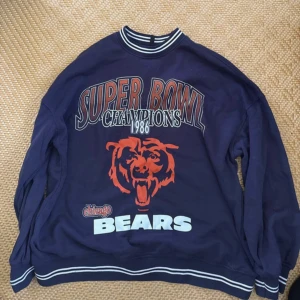 Sweatshirt - Säljer en mörkblå sweatshirt med stort Super Bowl Champions 1986-tryck och Chicago Bears-logga framtill. Tröjan har vita och svarta ränder på krage, ärmslut och nederkant. Som ny!!