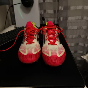 Adidas fotbollsskor i vitt och rött f50 - Säljer ett par Adidas fotbollsskor med snygg design i vitt, rött och gult. Skorna har röda snören, svarta ränder på sidan och gula detaljer vid hälen. Ovandelen är i syntetmaterial och sulan har dobbar för bra grepp på planen.