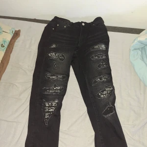 Svarta slime jeans med slitningar - Svarta jeans med slime fit och tydliga slitningar framtill. Byxorna har dragkedja, femficksmodell och är tillverkade i bomull med lite elastan för stretch. Snygga detaljer med trasiga partier och en modern look som passar till sneakers eller boots.