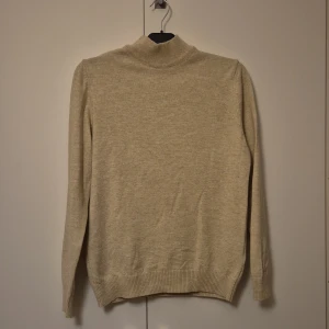 Beige polotröja från DeFacto M - Beige polotröja från DeFacto i storlek M. Tröjan är ribbstickad i halsen och har lång ärm. Tillverkad i 100% akryl, perfekt för lager på lager under kyliga dagar. Enkel och stilren design som passar till det mesta.