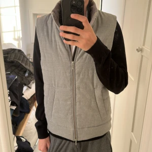 Grå väst Dressmann S - Säljer en grå dunväst från Dressmann i storlek S. Västen har quiltad design, ståkrage med ribbad insida och två fickor framtill. Stängs med dragkedja och är perfekt att slänga över en hoodie eller tröja för extra värme. Lite noppig längst nere vid mudden skickar fler bilder om de behövs 