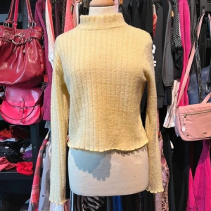 Gul ribbad tröja från Gina Tricot - Superfin ljusgul stickad ribbad tröja från Gina Tricot med lång ärm och hög hals. Tröjan har en mjuk, fluffig känsla och vågig kant nertill och vid ärmslut. Tyget har en fin skimmrande/glittrig effekt! Mer än M än en L i storleken 