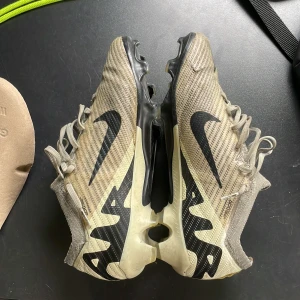 Nike mercurial vapor 15 elite - Säljer ett par Nike Air Zoom Mercurial fotbollsskor i beige och svart. Skorna har snörning, platt sula med dobbar och stor Nike-logga på sidan. Ovandelen är i syntetmaterial med textilstruktur för extra grepp och lätt känsla. Perfekta för dig som vill ha snabbhet och kontroll på planen. De har en liten skada på yttersta lagret som ni kan se på sista bilden men den påverkar inte hur skorna känns eller presterar på planen