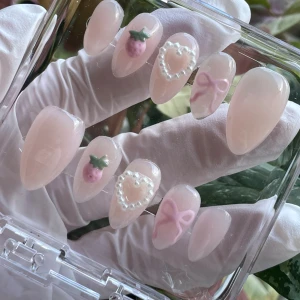Söta press-on naglar med jordgubbar & rosetter - Set med långa, mandelformade press-on naglar i ljusrosa. Dekorerade med 3D-detaljer som små rosa jordgubbar, pärlformade hjärtan och ljusrosa rosetter. Kommer i genomskinlig ask. Perfekt för dig som gillar gulliga och kreativa naglar.