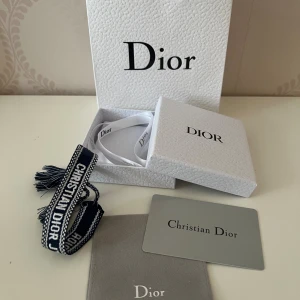 Christian Dior armband i blått och vitt - Snyggt armband från Christian Dior i marinblått och vitt med tydlig logga och tofsar i ändarna. Kommer i original ask och med äkthetskort. Perfekt accessoar för dig som vill ha en exklusiv och trendig detalj till din outfit.