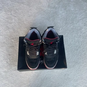 Nike Air Jordan 4 Black/Red - Säljer ett par ikoniska Nike Air Jordan 4 i svart mocka med röda och grå detaljer som är ganska använda. Skorna har klassisk meshpanel, snörning och synlig Air-sula. Röd Jumpman-logga på plösen och Nike Air-brodyr på hälen. Perfekt för dig som vill sticka ut med en tidlös sneaker. Skriv om du har en fråga!