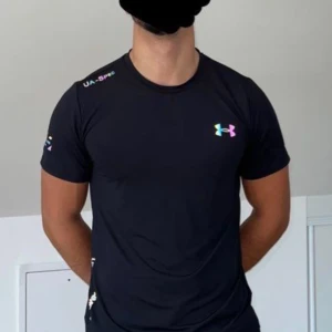 Svart Under Armour t-shirt i polyester - Svart t-shirt från Under Armour med färgglad logga på bröstet och tryck på ärmen och sidan. Tillverkad i mjuk och lätt polyester, perfekt för träning. Klassisk passform med korta ärmar och rund hals. Snygg och sportig stil för dig som gillar att sticka ut.