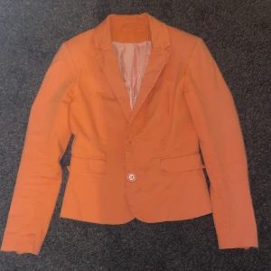 Orange kavaj - 🧡Snygg orange/aprikos kavaj med klassisk krage och två knappar framtill. Fodret är randigt i vitt och orange, fickorna är slutna och knappar finns vid ärmslut. Materialet känns som bomull och passformen känns som S exakt, varken större eller mindre.
