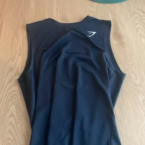 Svart linnetopp från Gymshark - Svart linnetopp från Gymshark i storlek S. Toppen är ärmlös och har en stilren design med Gymshark-logga på ryggen. Tillverkad i ett syntetmaterial som är perfekt för träning och ger en skön, tight passform. Perfekt för dig som gillar sportiga och funktionella plagg.