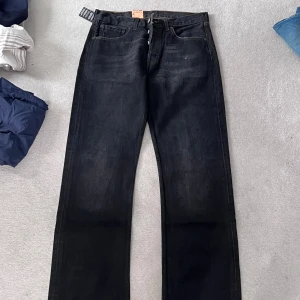 Levi's 501 svarta jeans 31/34 - Svarta Levi's 501 jeans med klassisk rak passform och knäppning framtill. Jeansen har fem fickor, tydliga sömmar och originaletiketter kvar. Tillverkade i robust denim som ger en tidlös look. ALDRIG ANVÄNDA