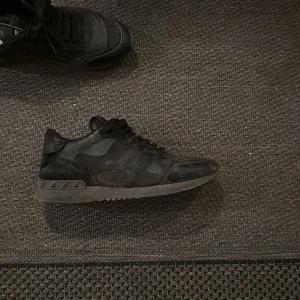 Svarta sneakers med snörning - Snygga svarta sneakers med låg profil och klassisk snörning. Skorna har en rund tå och platt sula, vilket gör dem perfekta för en avslappnad stil. Materialet ser ut att vara en mix av skinn och syntet för en cool look.