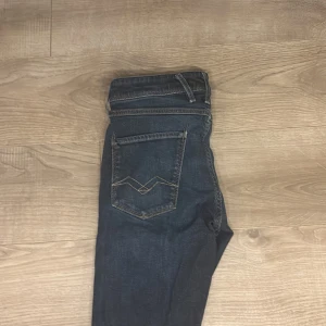 Replay Anbass jeans slim fit blå - Snygga Replay Anbass jeans i slim fit med klassisk femficksdesign och coola detaljer på fickorna. Färgen är mörkblå med lätt tvättad look och kontrastsömmar. Perfekt passform för dig som gillar smalare jeans med modern stil.