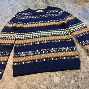 Mönstrad stickad tröja från Bonpoint - Stickad tröja från Bonpoint i marinblått med mönster i beige, vitt och blått. Tröjan har rund hals, långa ärmar och klassiskt nordiskt mönster. Storlek 12 år. Obs! Bonpoint är liten i storleken.