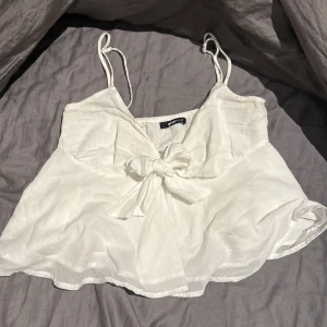 Vit linnetopp med rosett från Gina Tricot - Supersöt vit linnetopp från Gina Tricot i storlek XS. Toppen har tunna axelband, en stor rosett framtill och är tillverkad i ett luftigt linnematerial.