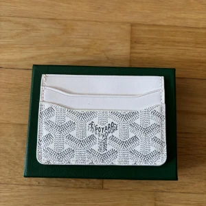 Vit Goy4rd Plånbok - Supersnyggt vitt kortfodral från Goy4rd med deras ikoniska mönster och logga. Fodralet har flera kortfack och är gjort i exklusivt skinn med ett diskret, stilrent print. Perfekt för dig som vill ha något både lyxigt och praktiskt i fickan.