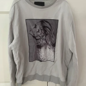 Grå sweatshirt från Limitato x Riocam - Säljer en grå sweatshirt från Limitato x Riocam med ett stort svartvitt fotoprint framtill. Tröjan har rund halsringning, långa ärmar och ribbade muddar. Limitato-logga broderad på ryggen. Perfekt för dig som gillar unika prints och streetstyle.