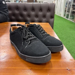 Svarta sneakers från Louboutin - Snygga svarta sneakers från Louboutin med klassisk röd sula och diskret logga undertill. Skorna har rund tå, snörning och ovandel i mocka för en lyxig känsla. Perfekta för dig som vill ha en stilren men ändå statement look.