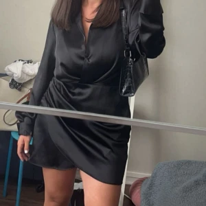 Svart omlottklänning från Zara - Snygg svart omlottklänning från Zara i glansigt satintyg. Klänningen har lång ärm, v-ringning✨