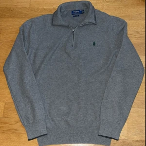 Grå halvzip tröja Polo Ralph Lauren - Grå långärmad tröja från Polo Ralph Lauren i 100% pima bomull. Klassisk modell med halv dragkedja och broderad grön logga på bröstet.
