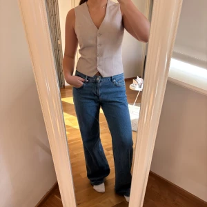 Beige v-ringad väst från Gina Tricot - Stilren beige väst från Gina Tricot med v-ringning och fyra knappar framtill. Västen har en klassisk, rak passform och är tillverkad i ett lätt tyg som ger en dressad look. Helt ny, aldrig använd, lappen sitter kvar, den är lite mindre i storlek så passar absolut S men även M. Aldrig använd!