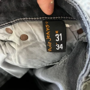 Nudie Jeans Skinny Lin grå jeans - Säljer ett par Nudie Jeans Skinny Lin i färgen Shimmering Grey. De är skinny fit med klassiska bakfickor och diskret broderi. Materialet är 99% bomull och 1% elastan för stretchig känsla. Perfekta om du gillar smala, mörkgrå jeans med stilren look.