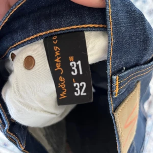 Nudie Jeans Thin Finn mörkblå jeans - Mörkblå Nudie Jeans Thin Finn med klassiska kontrastsömmar och broderade bakfickor. Jeansen är tillverkade av 98,5% ekologisk bomull och 1,5% elastan för en bekväm stretchig känsla. Slimmad passform och snyggt smal siluett. Obs hål i jeansen dock en lagning!
