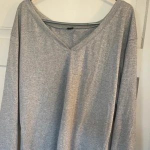 Grå v-ringad långärmad tröja - En enkel och stilren grå långärmad tröja med v-ringning. Tröjan har en avslappnad passform och är tillverkad i mjukt bomullsmaterial, perfekt för en chill och bekväm look.