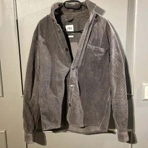 Grå manchester overahirt  - Säljer en grå manchesterskjorta från Zara i relaxed fit. Overshirten har tunna vertikala ränder, bröstficka och knäppning framtill. Perfekt oversized känsla och mjukt material som ger en chill vibe.
