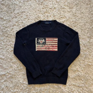 Mörkblå stickad tröja från Ralph Lauren - Riktigt snygg och unik stickad tröja från Ralph Lauren med en klassisk amerikansk flagga broderad på bröstet. Den är i mycket bra skick utan hål eller fläckar, storleken syns på bilden men jag skulle säga att den sitter som en M. Tveka inte på o skriva vid fler frågor!
