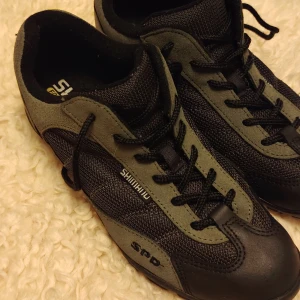 Shimano svartgröna cykelskor SPD strl 40 - Shimano cykelskor med SPD-fäste, svarta med mörkgrå detaljer i nyskick. Använda 1 gång men finns inga spår av bruksslitage. Snygg sportig design med snörning och robust gummisula. Ovandelen är i mesh och syntet för bra ventilation och komfort. Perfekt för dig som gillar att cykla med stil och funktion.