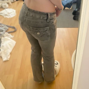 Grå bootcut jeans från Gina Tricot - Säljer ett par grå jeans från Gina Tricot i storlek 158. Jeansen har låg midja, bootcut-ben och snygga detaljerade bakfickor med knapp. Perfekta för dig som gillar en avslappnad men trendig look. Materialet är klassisk jeans med en lite tvättad finish.