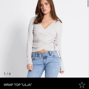 Beige omlottopp med knytband - Snygg beige omlottopp med långa ärmar och v-ringning. Toppen har knytband i sidan som ger en cool wrap-effekt och croppad passform. Perfekt att styla med jeans för en avslappnad look.